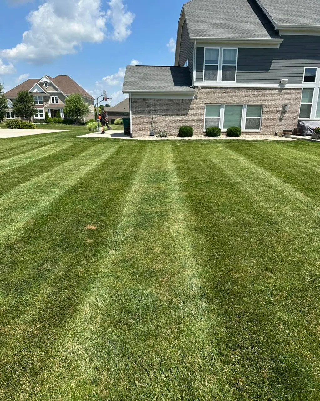 Fresh mowing stripes across the back lawn of a newer brick and siding home